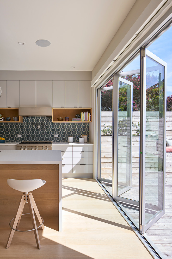 This is an example of a large contemporary kitchen in San Francisco with flat-panel cabinets, white cabinets, quartz benchtops, blue splashback, cement tile splashback, stainless steel appliances, light hardwood floors and with island.