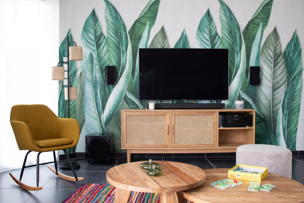 Foto på ett mellanstort tropiskt allrum med öppen planlösning, med ett bibliotek, gröna väggar, klinkergolv i keramik, en öppen vedspis, en väggmonterad TV och grått golv