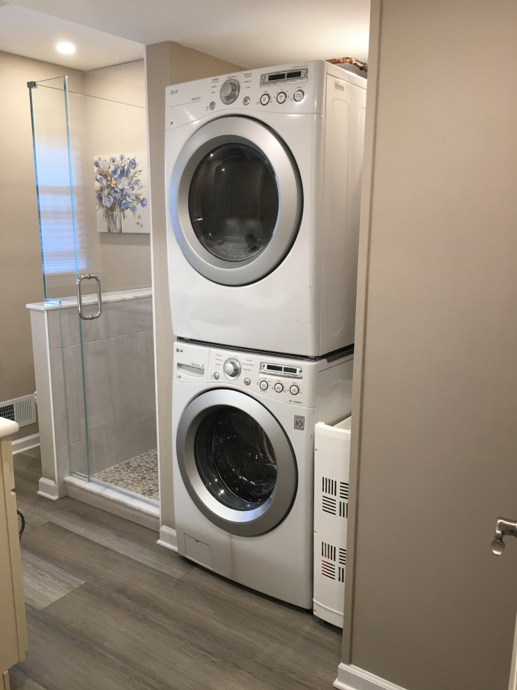 Photo of a small traditional galley utility room in New York with an undermount sink, raised-panel cabinets, beige cabinets, quartz benchtops, beige walls, vinyl floors, a stacked washer and dryer, grey floor and white benchtop.