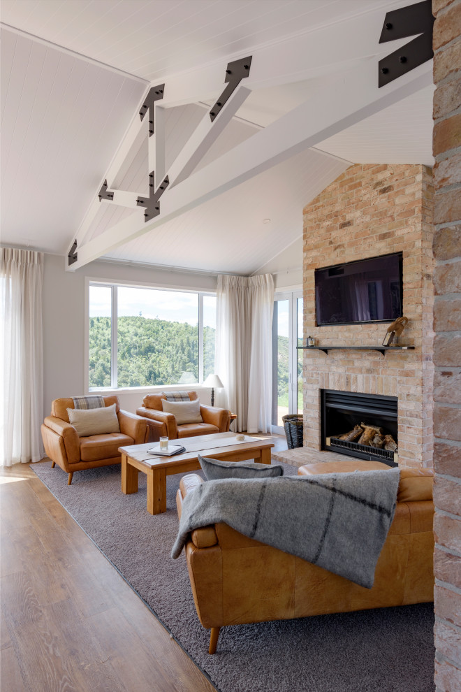 Country open concept living room in Sydney with white walls, medium hardwood floors, a standard fireplace, a brick fireplace surround, a wall-mounted tv, brown floor, exposed beam and vaulted.