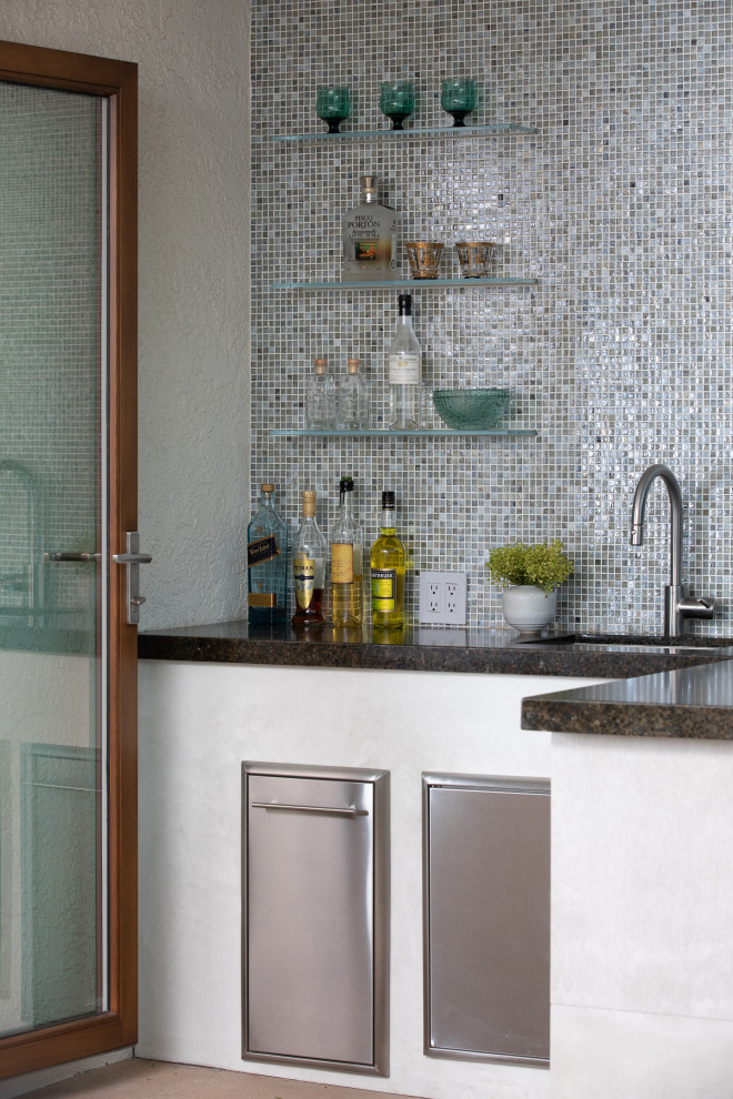 Photo of a mid-sized modern l-shaped wet bar in Los Angeles with an undermount sink, granite benchtops, blue splashback, mosaic tile splashback, concrete floors, beige floor and black benchtop.