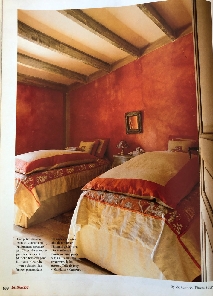 Cette image montre une chambre d'enfant méditerranéenne de taille moyenne avec un mur rouge, tomettes au sol, un sol beige et poutres apparentes.
