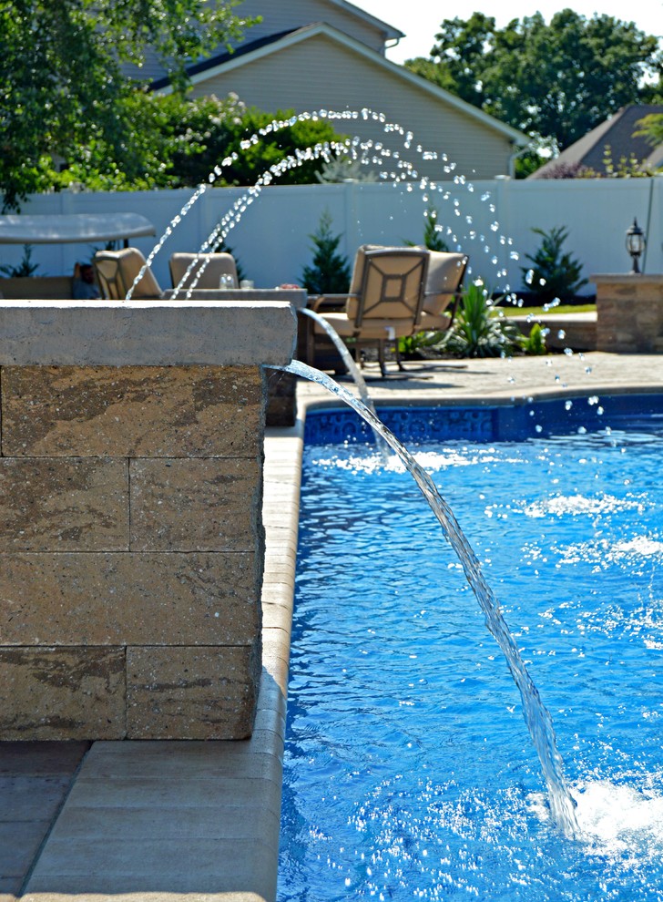 This is an example of a traditional backyard custom-shaped pool in New York with a water feature and concrete pavers.