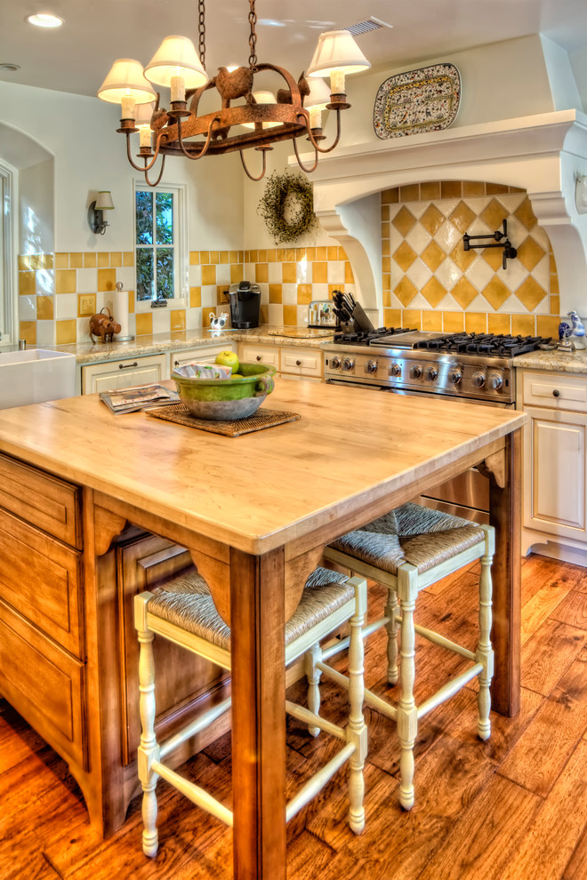 Mediterranean kitchen in Orange County with a farmhouse sink, raised-panel cabinets, beige cabinets, yellow splashback and stainless steel appliances.