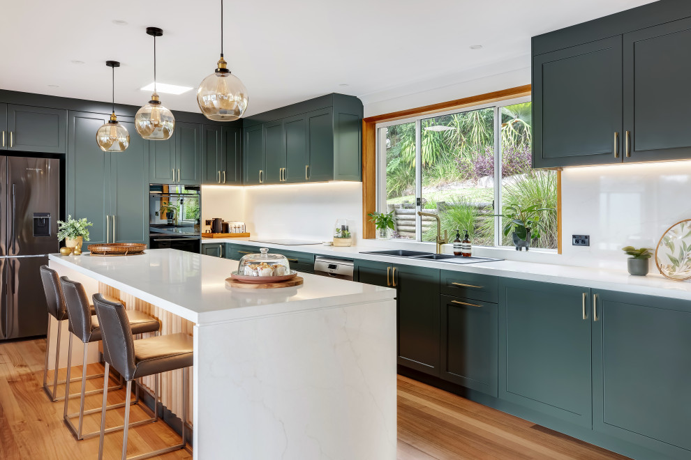 Large transitional l-shaped medium tone wood floor and multicolored floor eat-in kitchen photo in Sydney with a drop-in sink, shaker cabinets, green cabinets, quartz countertops, white backsplash, quartz backsplash, black appliances, an island and white countertops