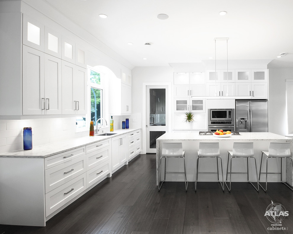 Design ideas for a large contemporary l-shaped eat-in kitchen in Vancouver with an undermount sink, shaker cabinets, white cabinets, quartzite benchtops, white splashback, porcelain splashback, stainless steel appliances, dark hardwood floors and with island.
