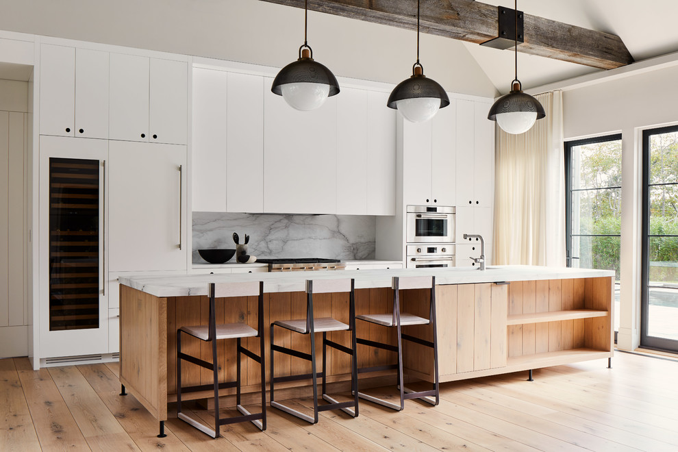 Design ideas for a beach style galley kitchen in New York with an undermount sink, flat-panel cabinets, white cabinets, grey splashback, stone slab splashback, panelled appliances, medium hardwood floors, with island, brown floor and white benchtop.