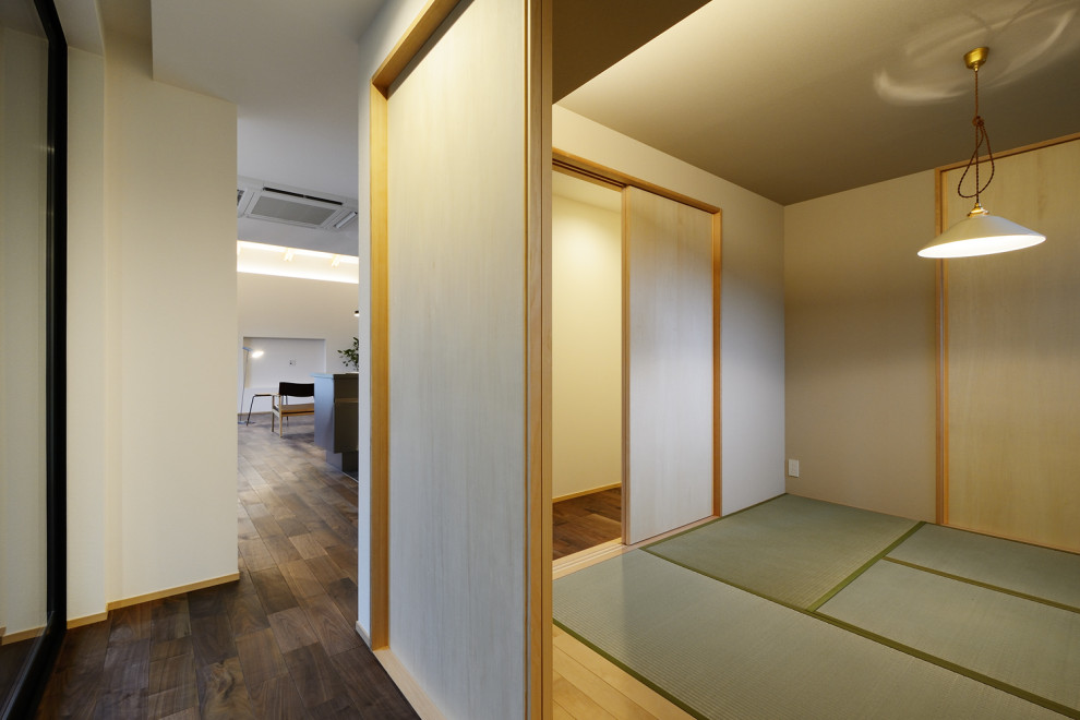 Minimalistisk inredning av ett mellanstort allrum, med vita väggar, tatamigolv, en fristående TV och grönt golv