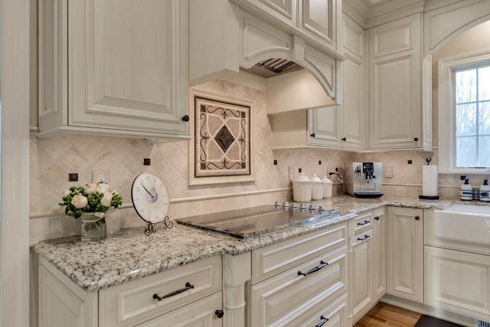 Inspiration for a large traditional kitchen in Baltimore with a farmhouse sink, raised-panel cabinets, granite benchtops, beige splashback, travertine splashback, stainless steel appliances, light hardwood floors and with island.