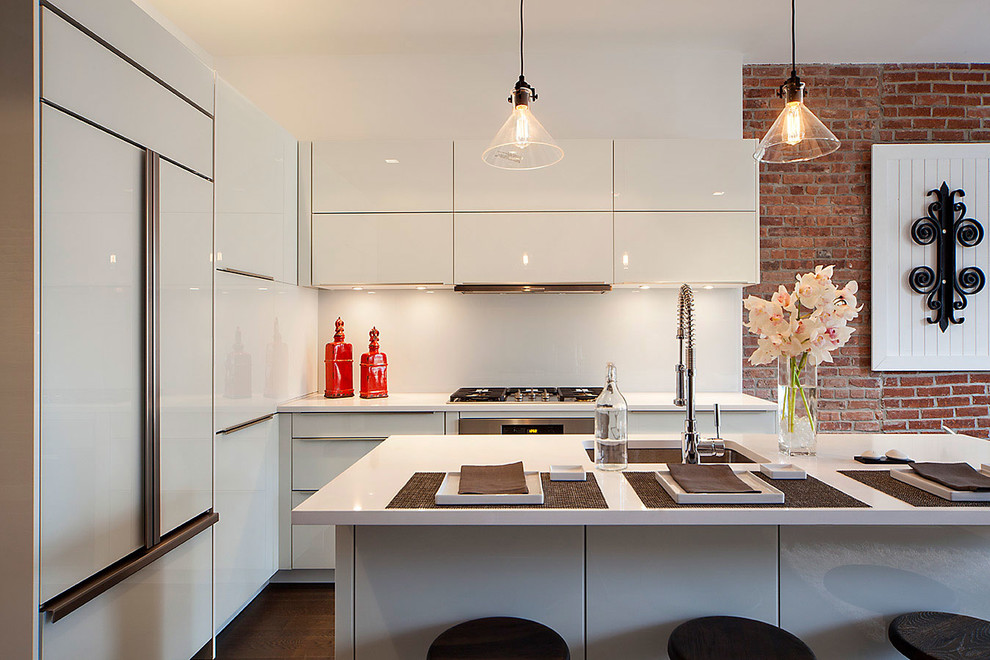 This is an example of an industrial kitchen in New York with an undermount sink, flat-panel cabinets, white cabinets, white splashback, panelled appliances, dark hardwood floors and with island.