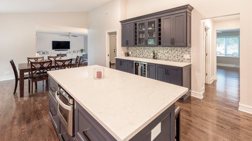 Mid-sized traditional l-shaped eat-in kitchen in Chicago with a double-bowl sink, shaker cabinets, white cabinets, quartz benchtops, white splashback, subway tile splashback, stainless steel appliances, medium hardwood floors, with island, brown floor and white benchtop.