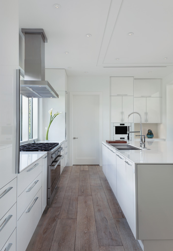Inspiration for a contemporary l-shaped kitchen in Miami with an undermount sink, flat-panel cabinets, white cabinets, stainless steel appliances, medium hardwood floors, with island, brown floor and white benchtop.