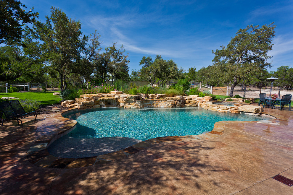Photo of a large country backyard custom-shaped natural pool in Austin with a water feature and concrete slab.
