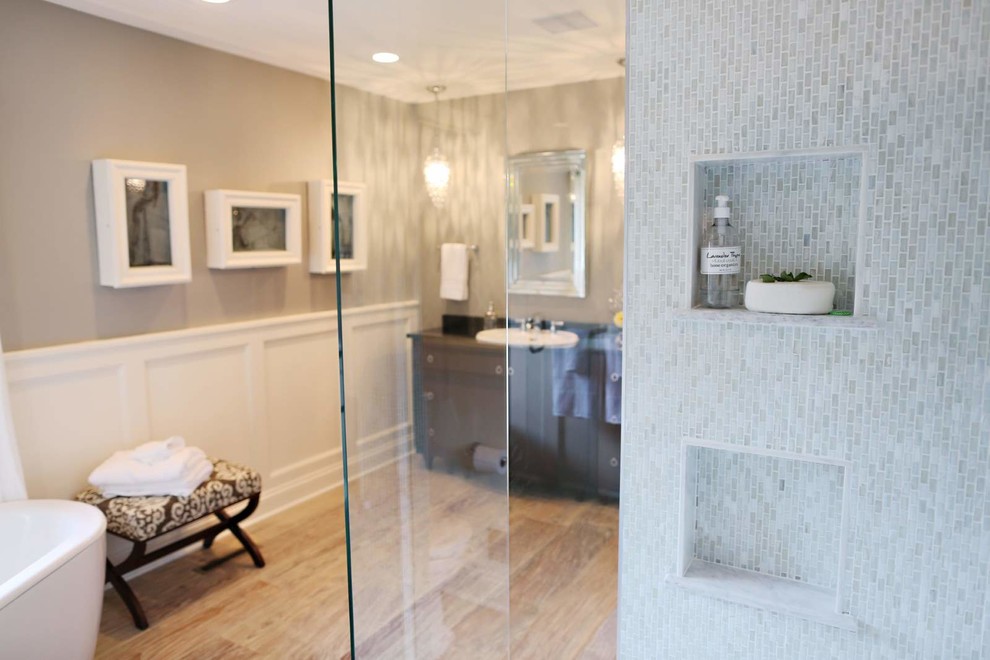 Example of a small transitional master gray tile and matchstick tile light wood floor and beige floor freestanding bathtub design with furniture-like cabinets, brown cabinets, a one-piece toilet, beige walls, a drop-in sink, laminate countertops and a hinged shower door