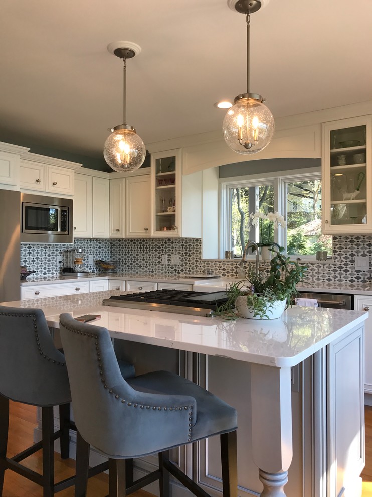 Mid-sized transitional l-shaped medium tone wood floor and brown floor eat-in kitchen photo with a farmhouse sink, recessed-panel cabinets, white cabinets, marble countertops, gray backsplash, mosaic tile backsplash, stainless steel appliances and an island