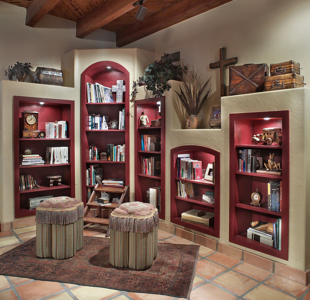 This is an example of an open concept living room in Phoenix with a library, white walls and terra-cotta floors.