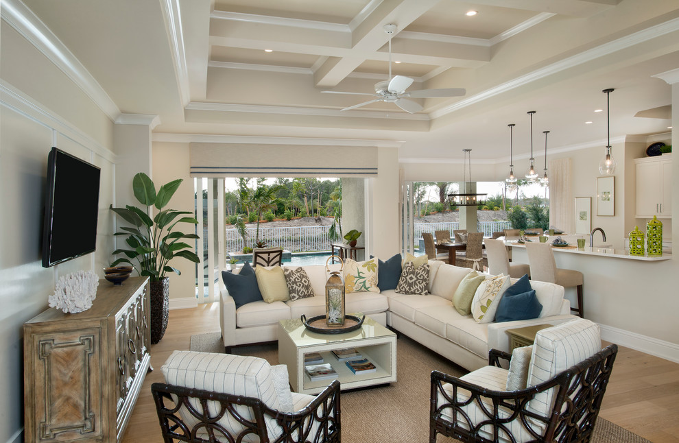Photo of a mid-sized tropical open concept family room in Miami with beige walls, light hardwood floors, no fireplace, a wall-mounted tv and brown floor.