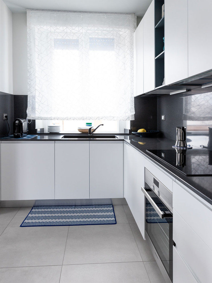 Photo of a mid-sized modern l-shaped open plan kitchen in Other with an integrated sink, flat-panel cabinets, white cabinets, marble benchtops, black splashback, stainless steel appliances, porcelain floors, grey floor, black benchtop, recessed, no island and marble splashback.