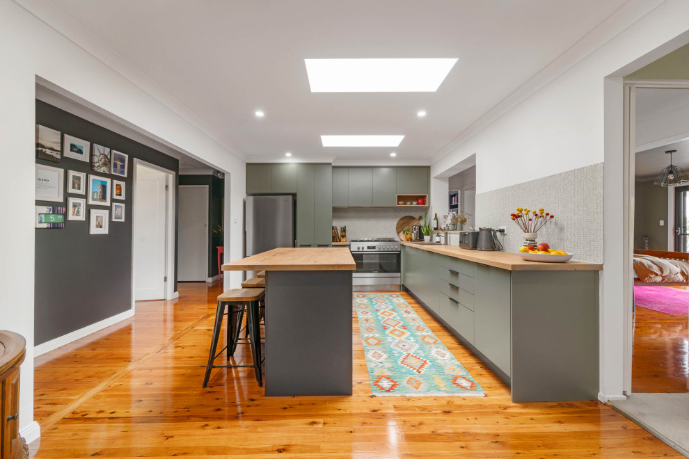 Design ideas for a mid-sized contemporary l-shaped kitchen pantry in Sydney with a drop-in sink, flat-panel cabinets, green cabinets, wood benchtops, grey splashback, cement tile splashback, stainless steel appliances, light hardwood floors, with island and brown benchtop.