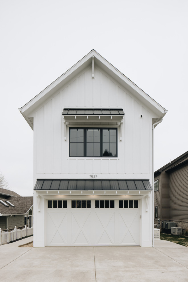 This is an example of a large beach style white house exterior in Grand Rapids with four or more storeys, a gable roof, a mixed roof, a black roof and board and batten siding.