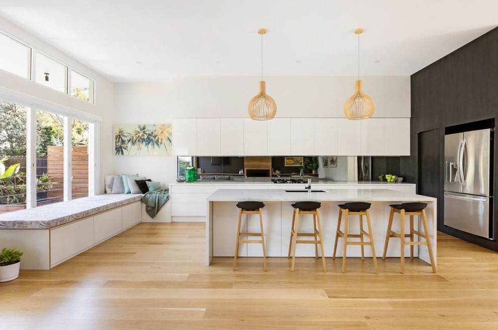 Design ideas for a contemporary l-shaped kitchen in Sydney with an undermount sink, flat-panel cabinets, white cabinets, mirror splashback, stainless steel appliances, light hardwood floors, with island, beige floor and white benchtop.