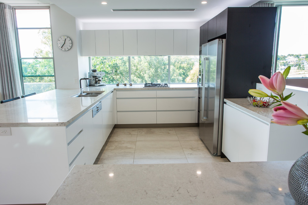 Photo of a large contemporary u-shaped open plan kitchen in Brisbane with a double-bowl sink, recessed-panel cabinets, white cabinets, solid surface benchtops, stainless steel appliances, porcelain floors, multiple islands, brown floor and brown benchtop.