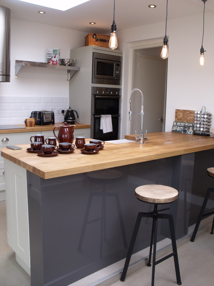 Expansive contemporary u-shaped eat-in kitchen in Devon with an undermount sink, louvered cabinets, beige cabinets, wood benchtops, white splashback, ceramic splashback, stainless steel appliances, vinyl floors and a peninsula.