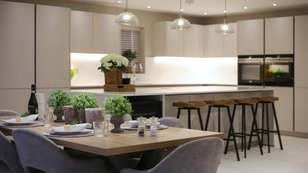 Large scandinavian single-wall open plan kitchen in Hertfordshire with a single-bowl sink, flat-panel cabinets, white cabinets, quartz worktops, white splashback, black appliances, an island, white floors, white worktops and feature lighting.