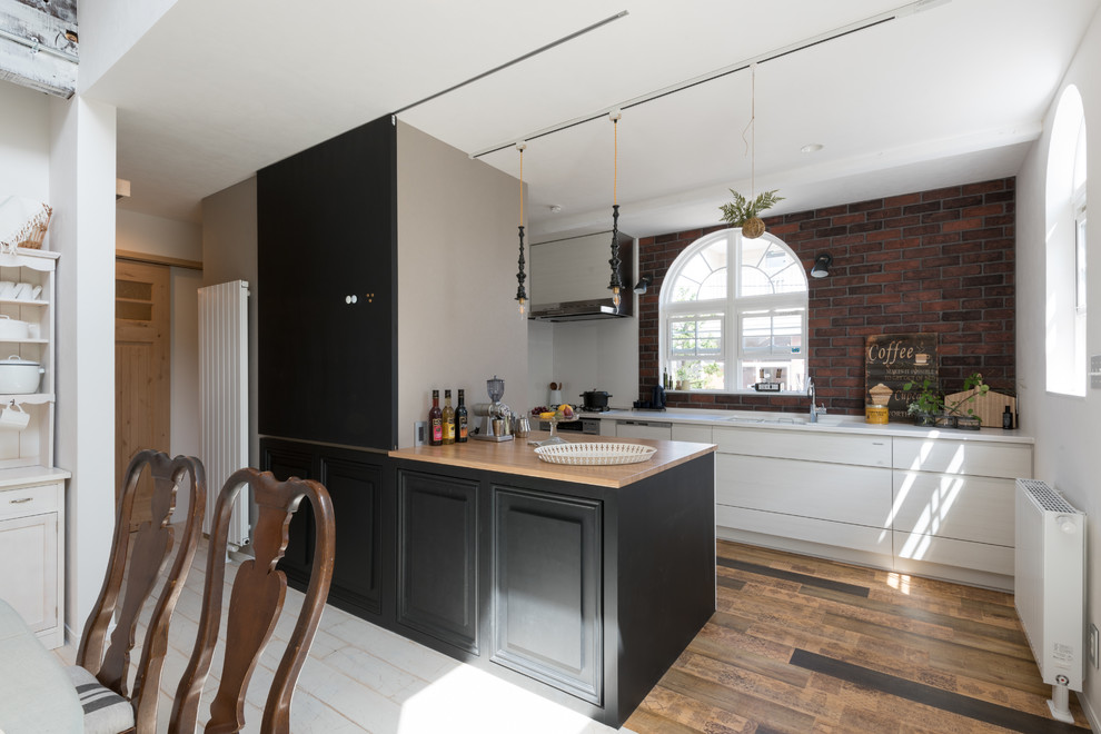 This is an example of a contemporary single-wall eat-in kitchen in Sapporo with an integrated sink, flat-panel cabinets, white cabinets, brown splashback, brick splashback, painted wood floors, a peninsula, brown floor and black benchtop.
