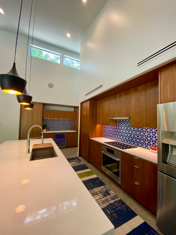 ヒューストンにある広いモダンスタイルのおしゃれなキッチン (アンダーカウンターシンク、フラットパネル扉のキャビネット、中間色木目調キャビネット、クオーツストーンカウンター、青いキッチンパネル、セラミックタイルのキッチンパネル、シルバーの調理設備、コンクリートの床、グレーの床、白いキッチンカウンター) の写真
