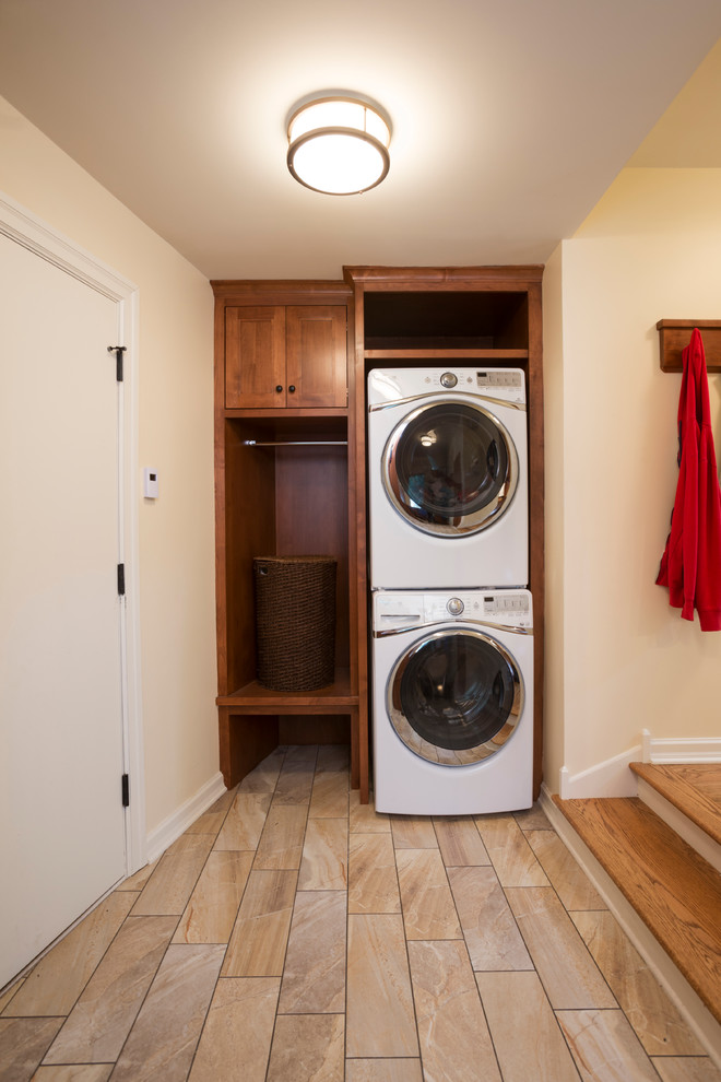 This is an example of a small traditional single-wall utility room in Minneapolis with recessed-panel cabinets, medium wood cabinets, beige walls, travertine floors and a stacked washer and dryer.