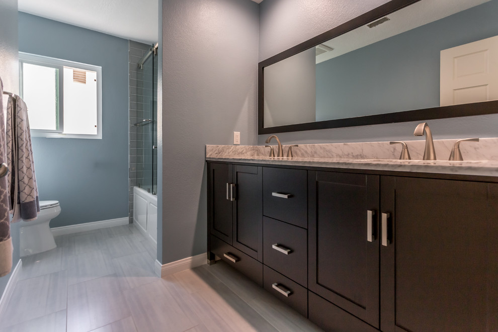 Large transitional 3/4 bathroom in Los Angeles with shaker cabinets, dark wood cabinets, an alcove tub, a shower/bathtub combo, gray tile, glass tile, blue walls, porcelain floors, an undermount sink and quartzite benchtops.