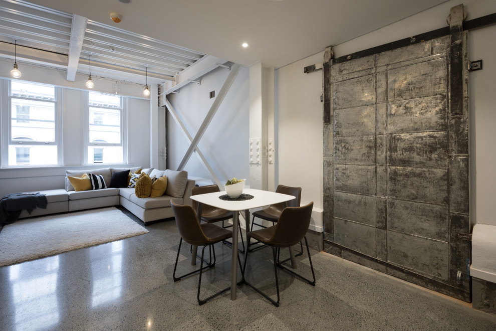 This is an example of an industrial open plan dining in Auckland with white walls, concrete floors and grey floor.