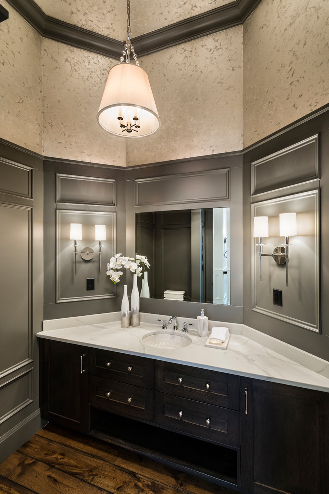 Inspiration for an expansive country powder room in Vancouver with shaker cabinets, dark wood cabinets, a two-piece toilet, grey walls, medium hardwood floors, an undermount sink, solid surface benchtops, brown floor and white benchtops.