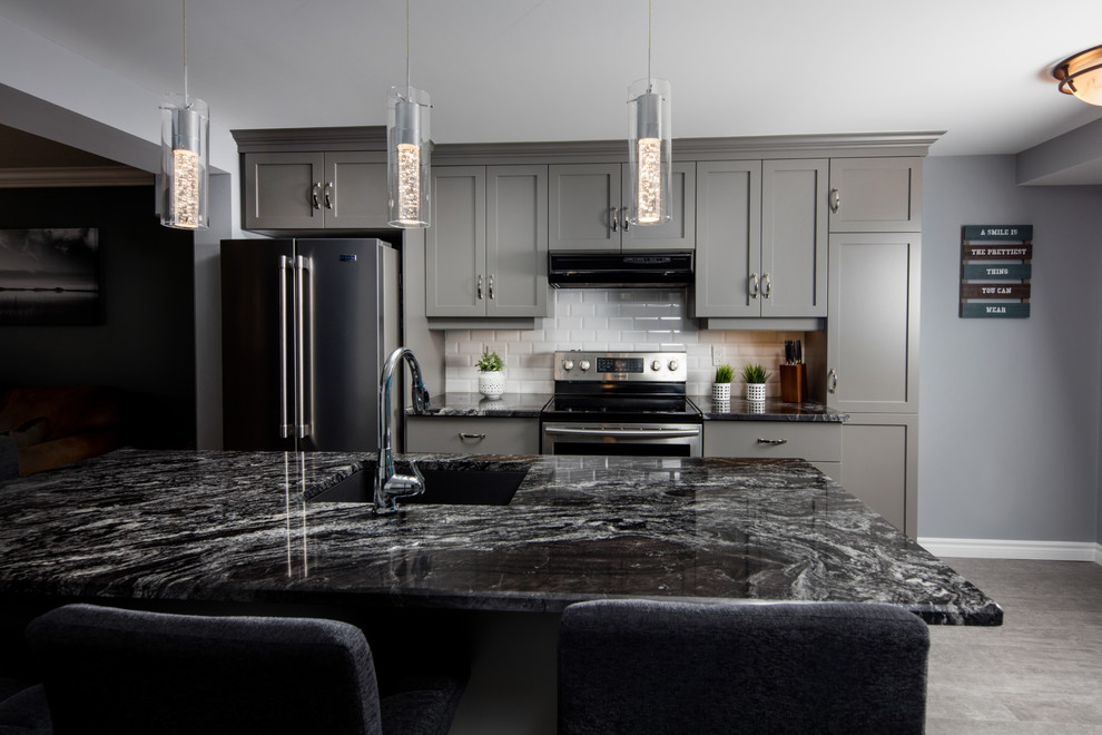 Example of a gray floor kitchen design in Toronto with shaker cabinets, gray cabinets, white backsplash, subway tile backsplash, stainless steel appliances, an island and black countertops