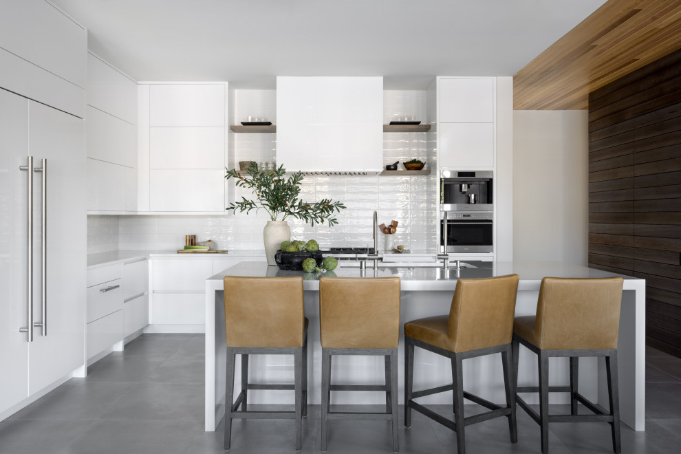 Moderne Küche in L-Form mit Unterbauwaschbecken, flächenbündigen Schrankfronten, weißen Schränken, Küchenrückwand in Weiß, Küchengeräten aus Edelstahl, Kücheninsel, grauem Boden und weißer Arbeitsplatte
