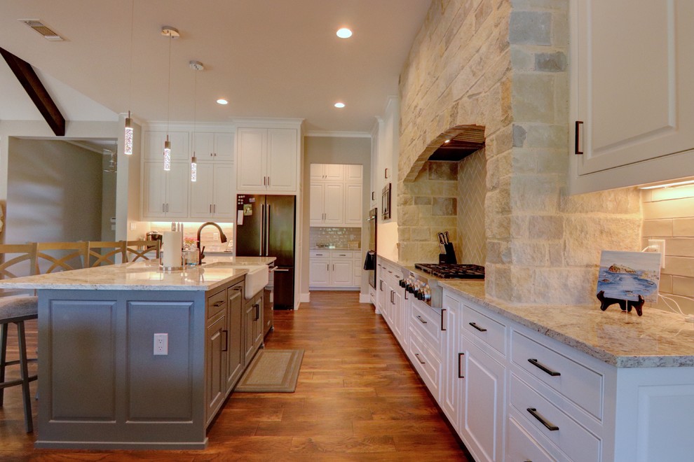 Eat-in kitchen - mid-sized transitional l-shaped medium tone wood floor and brown floor eat-in kitchen idea in Dallas with a farmhouse sink, raised-panel cabinets, white cabinets, granite countertops, white backsplash, ceramic backsplash, colored appliances, an island and gray countertops
