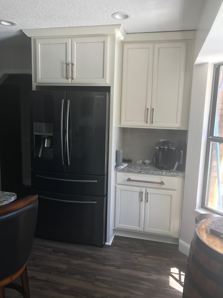 Photo of a large transitional open plan kitchen in Jacksonville with an undermount sink, shaker cabinets, white cabinets, granite benchtops, white splashback, glass tile splashback, black appliances, vinyl floors, with island, grey floor and white benchtop.