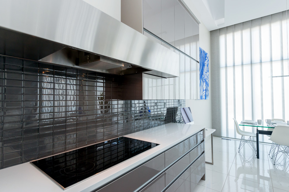 Photo of a large contemporary l-shaped eat-in kitchen in Calgary with an undermount sink, flat-panel cabinets, grey cabinets, quartz benchtops, grey splashback, glass tile splashback, stainless steel appliances, porcelain floors and with island.