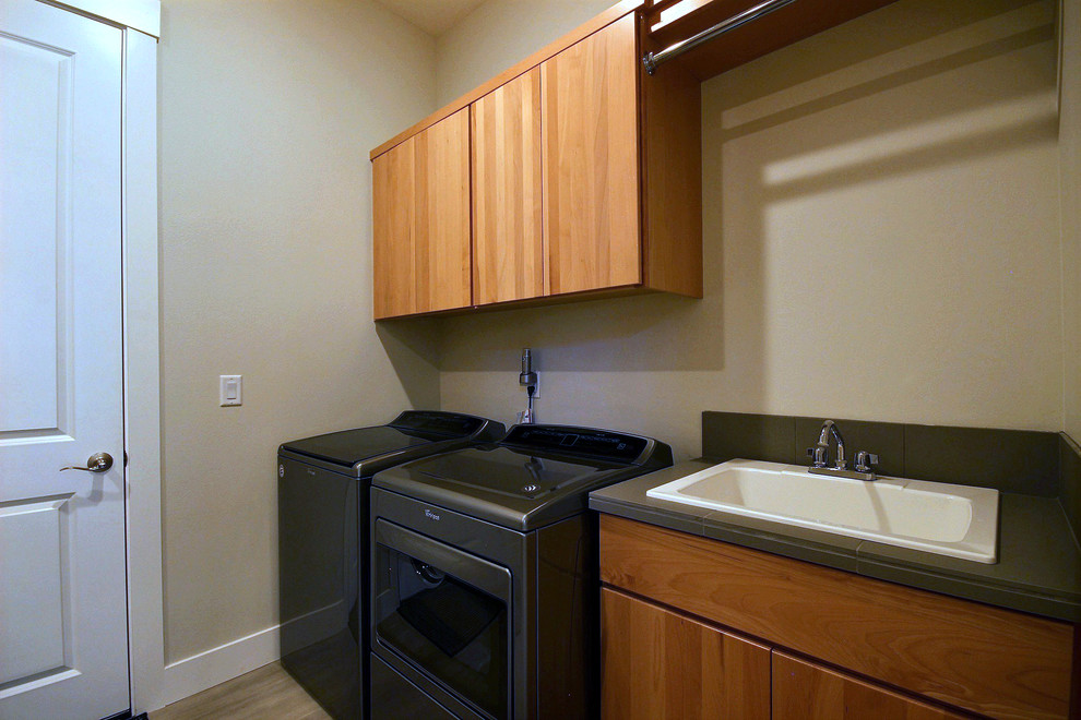Large modern galley dedicated laundry room in Portland with a drop-in sink, flat-panel cabinets, medium wood cabinets, wood benchtops, beige walls, porcelain floors, a side-by-side washer and dryer, beige floor and brown benchtop.