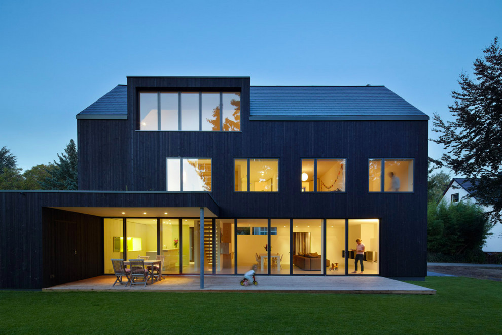 Large contemporary three-storey black exterior in Dusseldorf with wood siding and a gable roof.
