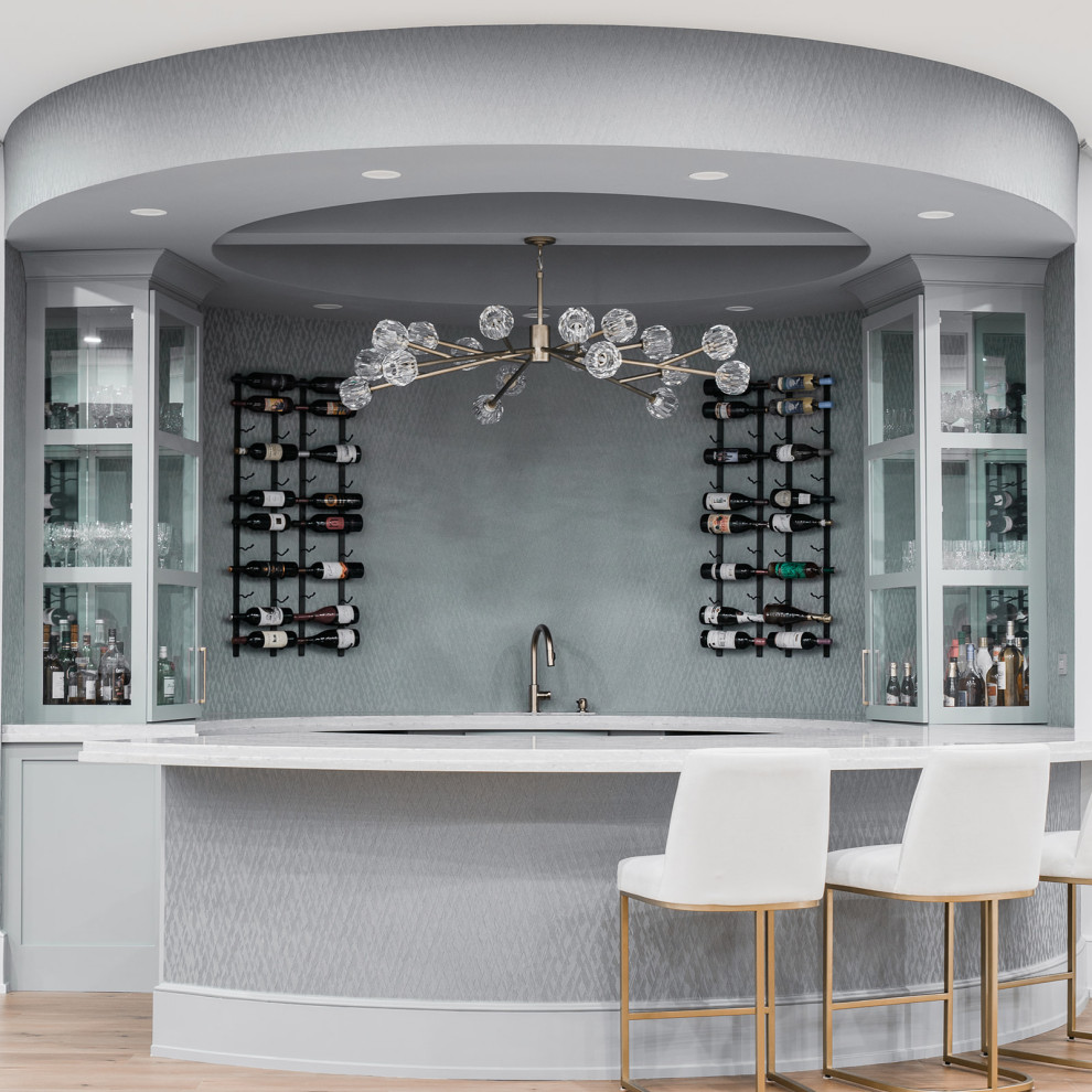 Photo of an expansive modern galley seated home bar in Chicago with an integrated sink, glass-front cabinets, grey cabinets, light hardwood floors, beige floor and grey benchtop.
