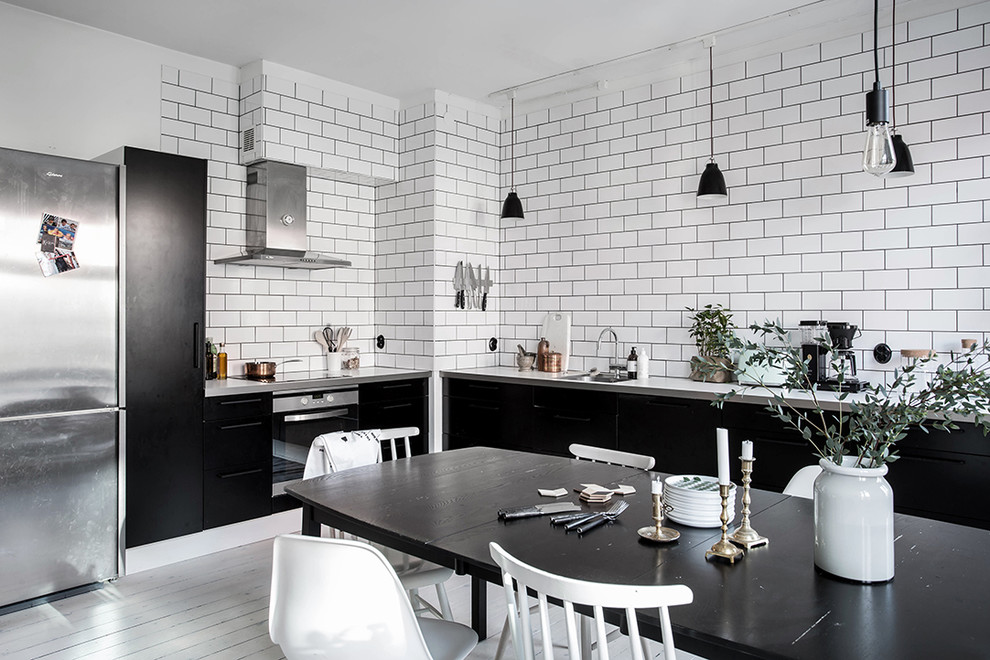 Photo of a large scandinavian l-shaped eat-in kitchen in Gothenburg with a single-bowl sink, flat-panel cabinets, black cabinets, stainless steel appliances, painted wood floors and with island.