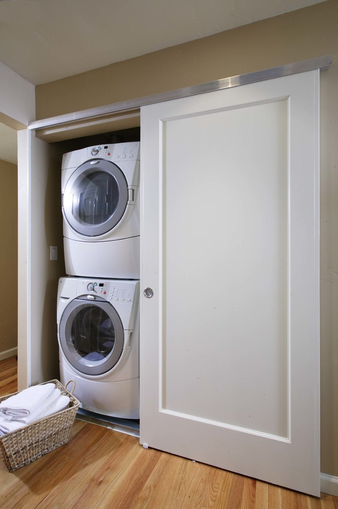 Small modern single-wall laundry cupboard in Sacramento with light hardwood floors, a stacked washer and dryer and beige walls.