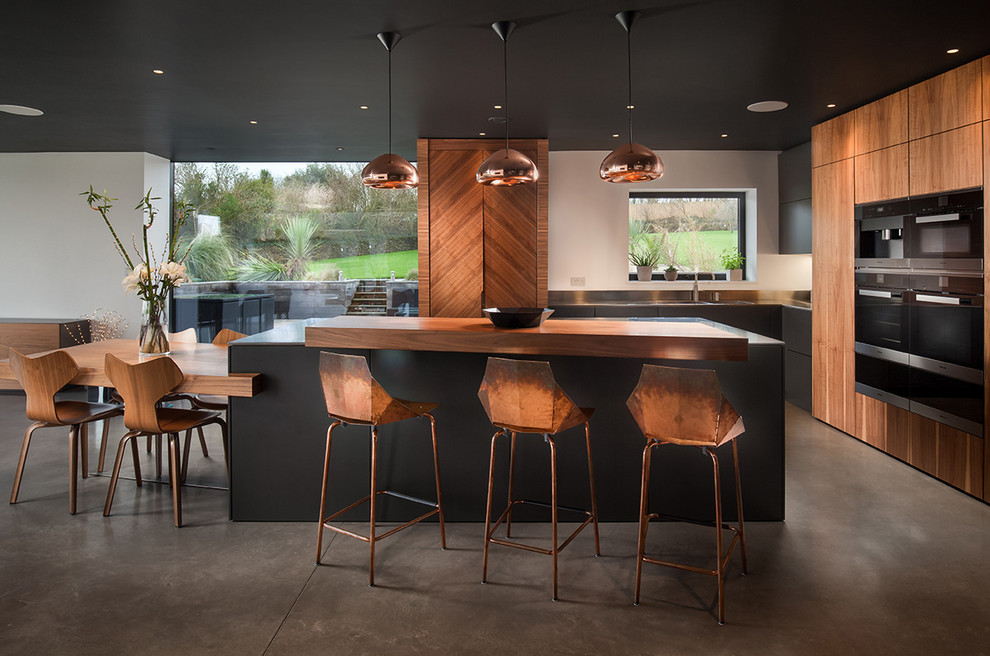Design ideas for a large contemporary l-shaped eat-in kitchen in Cornwall with flat-panel cabinets, medium wood cabinets, stainless steel benchtops, concrete floors, with island, grey floor, grey benchtop and panelled appliances.