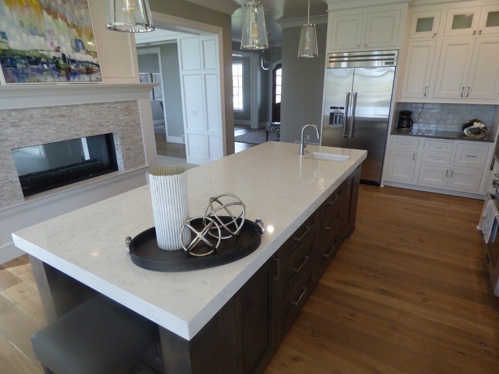 Example of a large transitional l-shaped light wood floor eat-in kitchen design with an undermount sink, recessed-panel cabinets, white cabinets, quartz countertops, white backsplash, subway tile backsplash, stainless steel appliances and an island