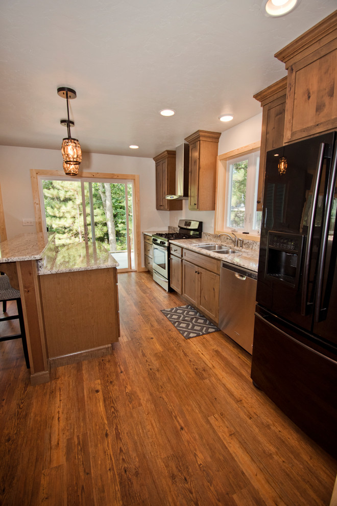 This is an example of a mid-sized country galley eat-in kitchen in Other with a double-bowl sink, recessed-panel cabinets, brown cabinets, granite benchtops, stainless steel appliances, medium hardwood floors, with island, brown floor and beige benchtop.