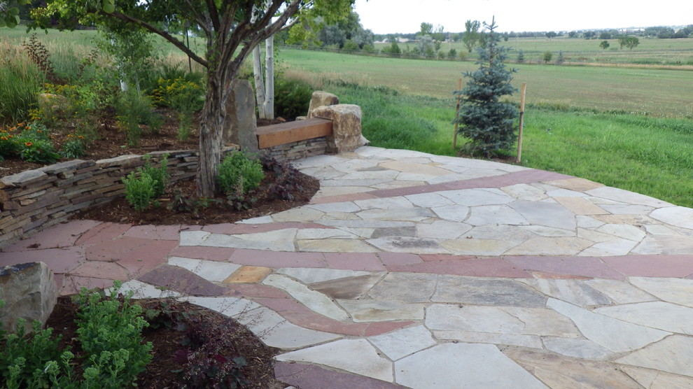 This is an example of a mid-sized country backyard patio in Denver with natural stone pavers and no cover.