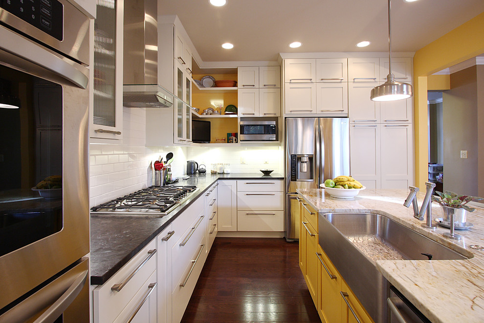 This is an example of a transitional kitchen in DC Metro with stainless steel appliances, yellow cabinets, a farmhouse sink, white splashback and subway tile splashback.