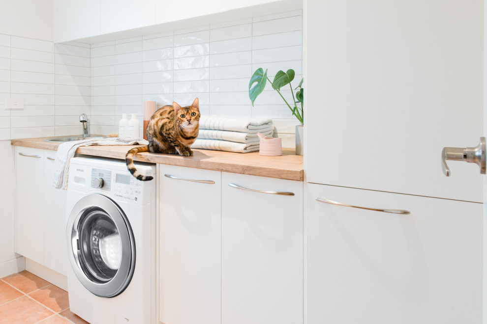 Inspiration for a mid-sized scandinavian galley dedicated laundry room in Melbourne with a drop-in sink, open cabinets, white cabinets, laminate benchtops, white walls, terra-cotta floors and a side-by-side washer and dryer.